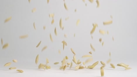 slivered raw almond nut pieces bouncing into pile on white backdrop in slow motion