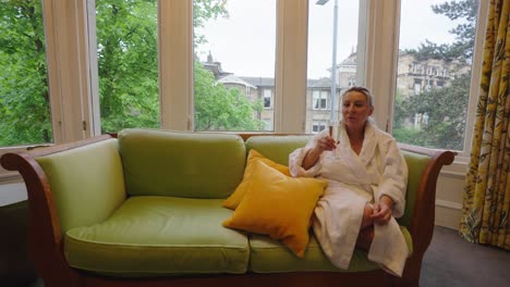 Woman-relaxes-on-sofa-wearing-dressing-gown-and-drinking-wine,-locked-off