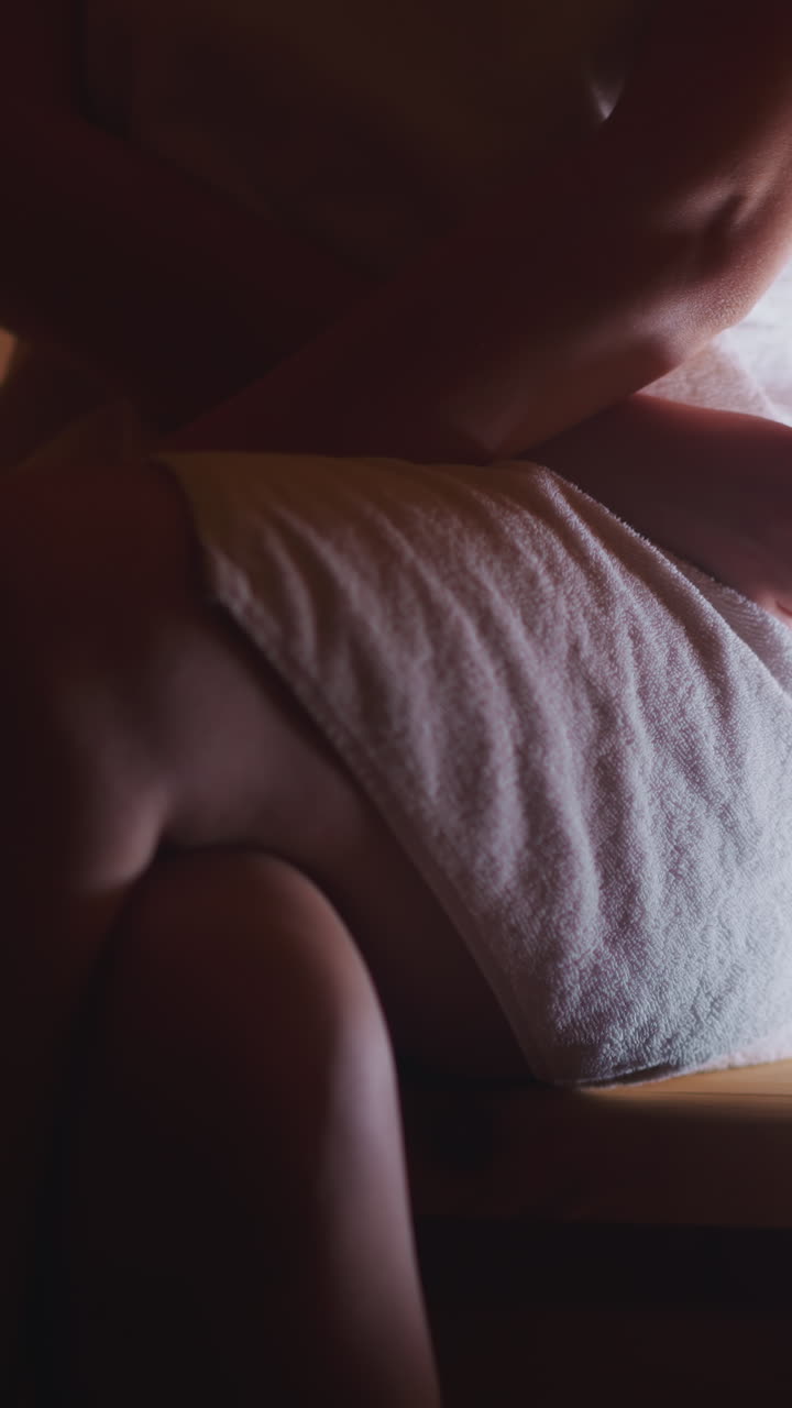 Woman sits on wooden bench in sauna closeup. Slim lady wrapped with bath towel enjoys hot procedures at spa center. Relaxing body care treatment