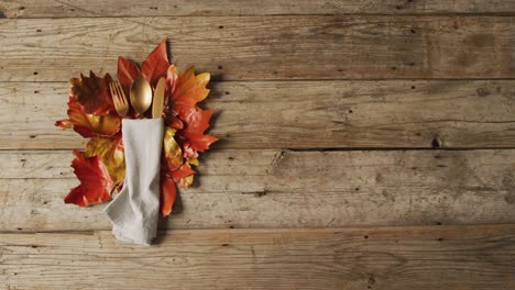 Video-of-cutlery,-cloth-and-autumn-decoration-with-leaves-lying-on-wooden-surface