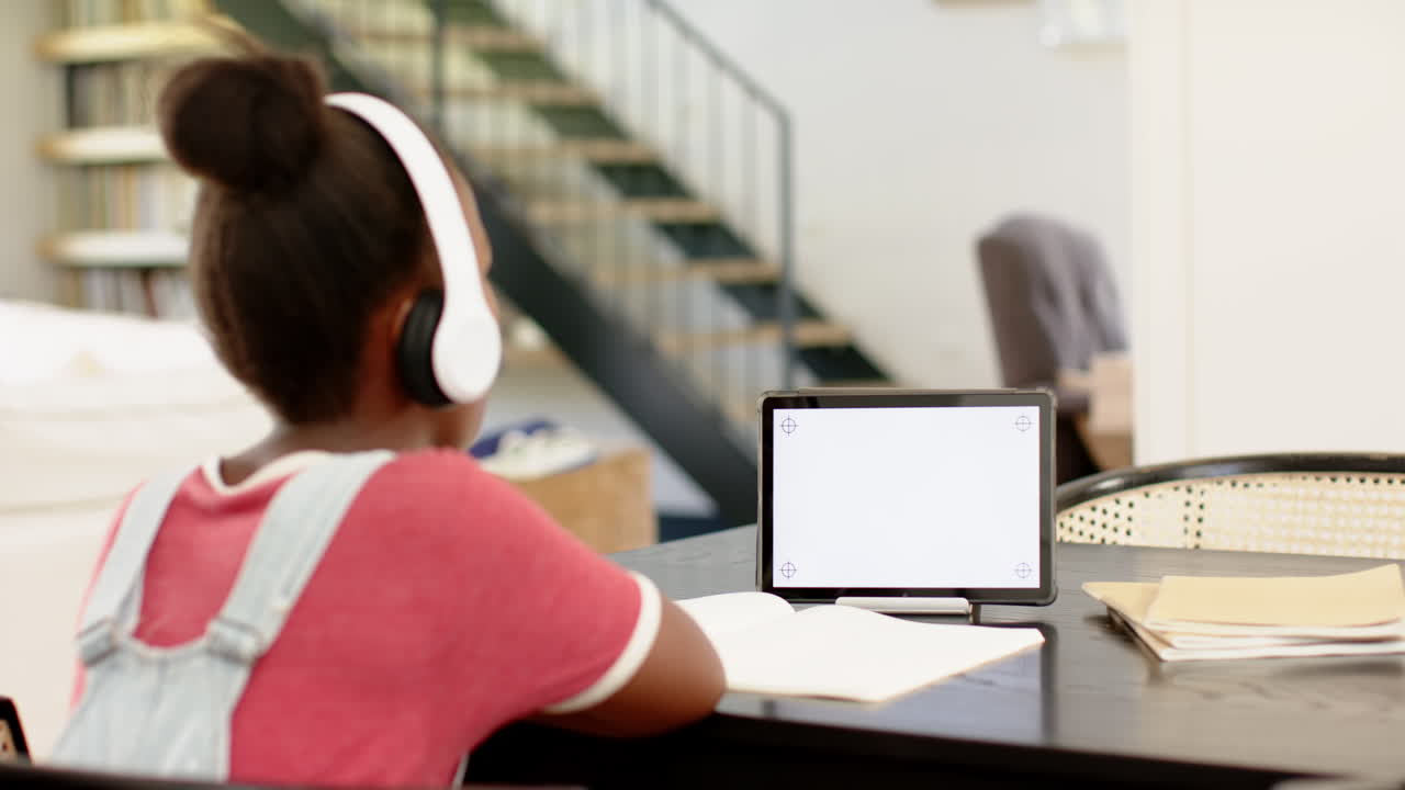 In school, child wearing headphones studying with tablet and notebook at desk, copy space