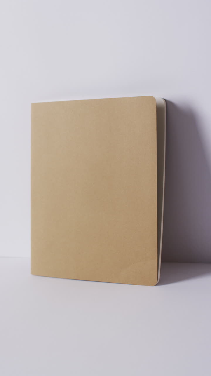 Vertical video of closed beige book leaning on wall with copy space in slow motion