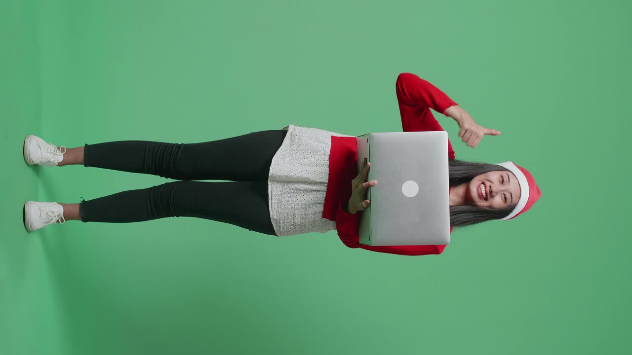 mujer con sombrero de santa con computadora portátil y pulgares hacia arriba