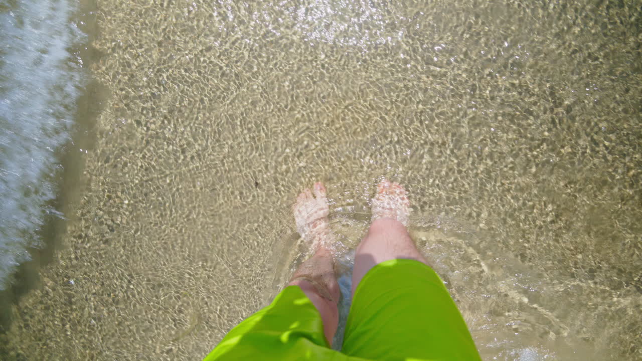 High angle view of a man's feet walking through shallow sea water on a sunny beach in Alicante, Spain