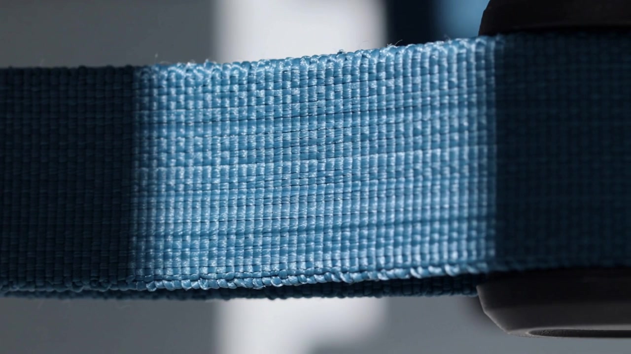 Luce in movimento che rivela una trama intrecciata su una cinghia azzurra vicino a una finestra luminosa, con una mano che tiene una fibbia.
