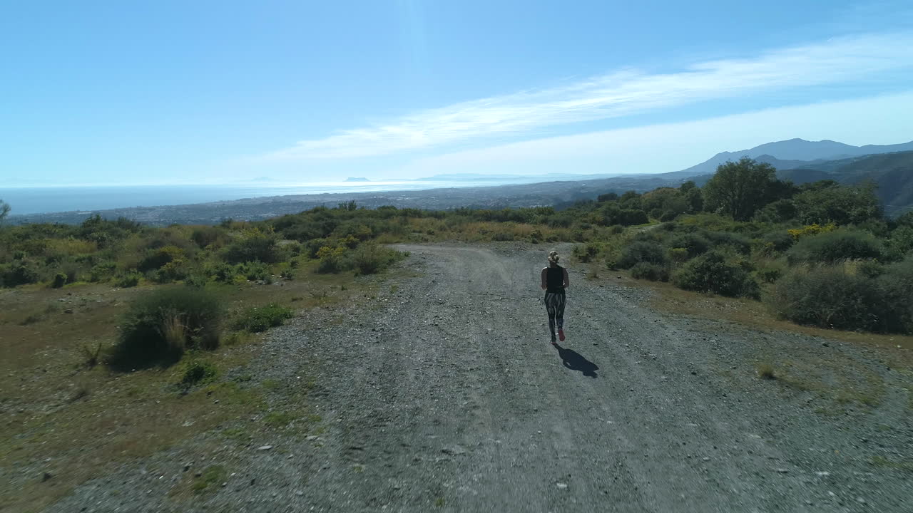 푸른 바다의 아름다운 전망을 보여주는 산속의 금발 여성 주자의 공중비행