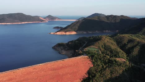 Toma-Aérea-En-Movimiento-Hacia-Adelante-Sobre-Una-Presa-Construida-Para-Conectar-El-Grupo-De-Islas-Habitadas-En-El-Parque-Geográfico-De-Hong-Kong-En-Sai-Kung-Al-Atardecer