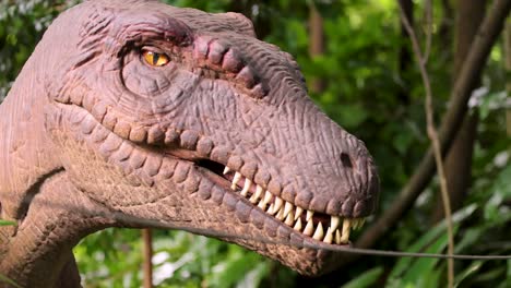 a realistic animatronic velociraptor head turns and blinks in a sunlit, green outdoor park environment, with close-up framing and natural lighting