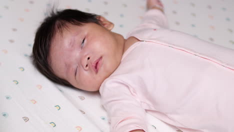 cute baby girl, 2 months old, with long black hair in a pink outfit, lying on a soft mattress after drinking milk, reflecting calmness and contentment