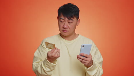 asian man using credit bank card and smartphone while transferring money purchases online shopping