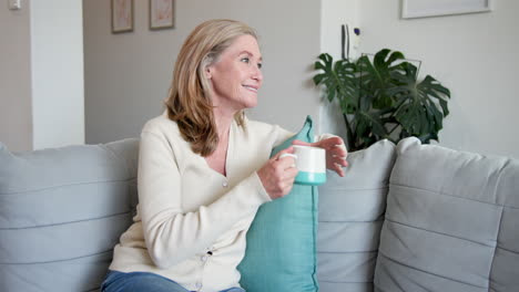 smiling senior woman relaxing on sofa with coffee at home, feeling content