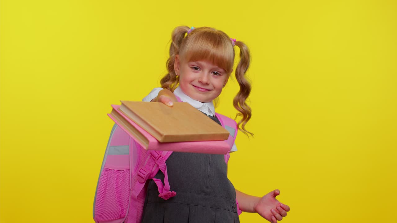 una estudiante alegre vestida con uniforme mostrando libros a la cámara, anima a estudiar juntos