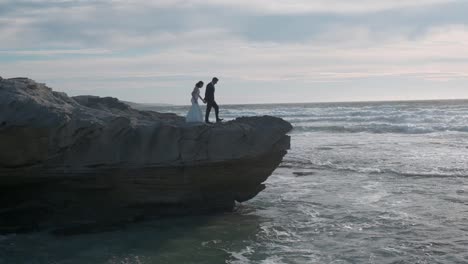 Married-couple-walk-hand-in-hand-onto-the-edge-of-a-cliff-by-the-ocean