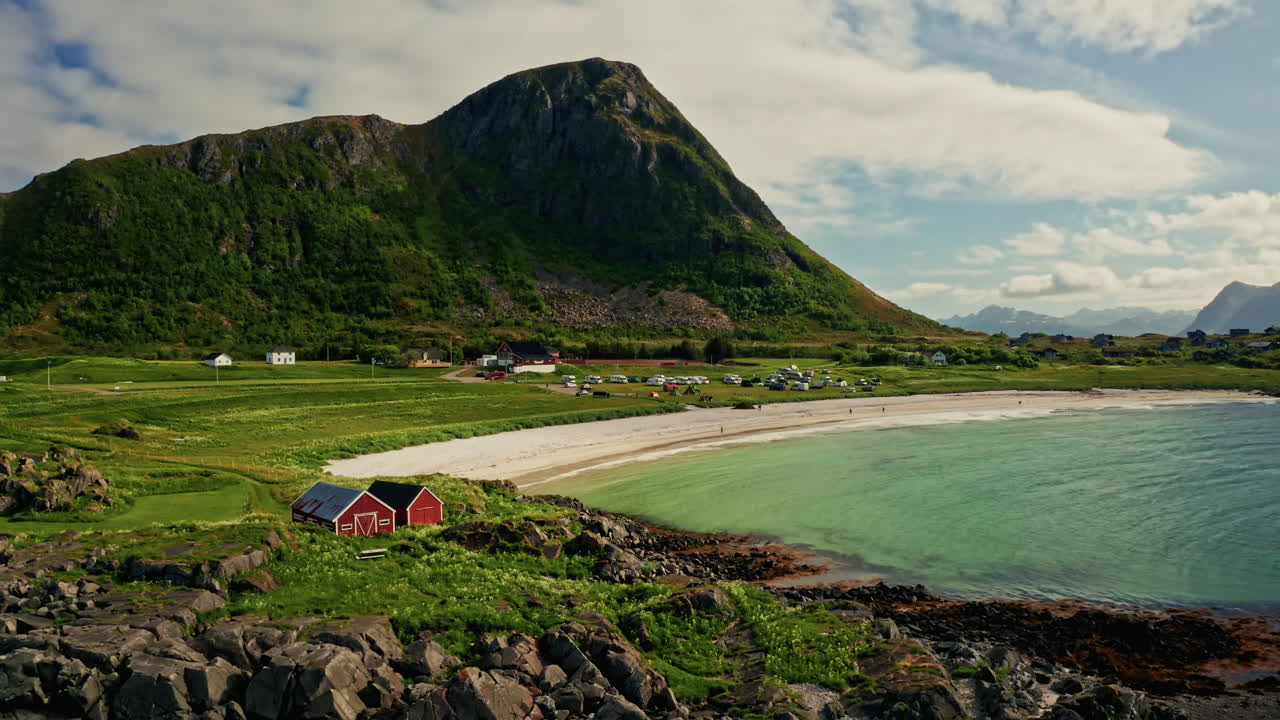 Aerial drone shot of the picturesque green landscape of the Lofoten islands, Norway. Bird's eye view of the white sanded beach, sea mountain in the background.