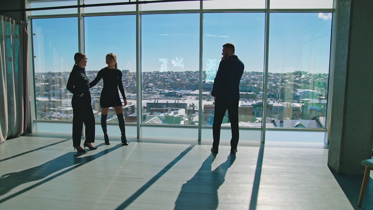Beautiful young ladies and businessman indoors. Business women and handsome entrepreneur standing at office windows during break.