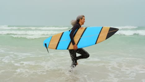 side view of active senior african american female surfer running towards sea on the beach 4k