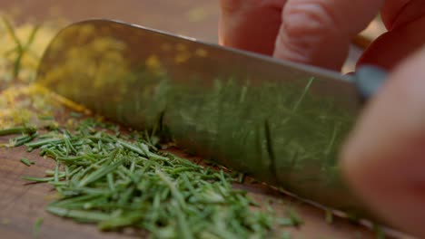 chef cortando hierbas frescas en una tabla de madera con un cuchillo grande