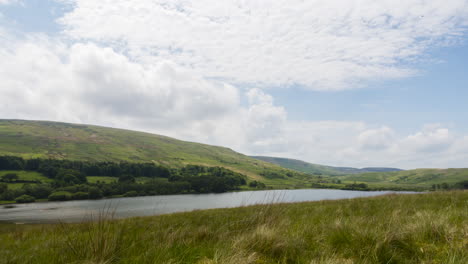 Time-lapse-of-the-clouds-moving-over-a-lake-surrounded-by-green-hills,-on-a-bright-summers-day