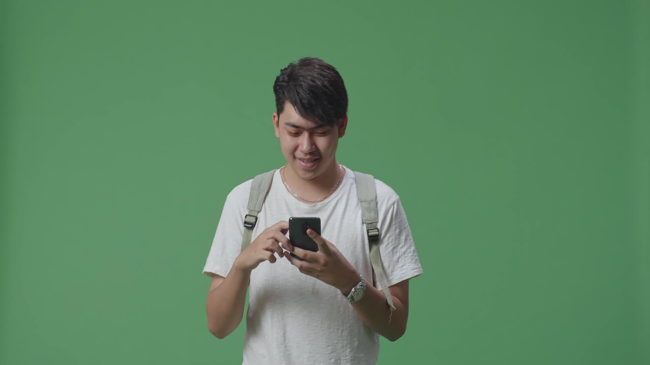 행복 한 아시아인 학생 은 녹색 스크린 스튜디오 에서 는 동안 휴대 전화 를 사용 하고 있다