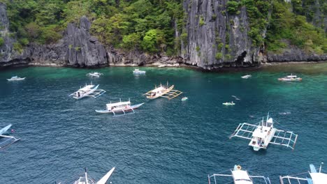 Multiple-Island-hopping-tour-boats-anchored-at-Cadlao-Lagoon,-El-Nido-in-Tropical-turquoise-water-of-Ubugon-Cove