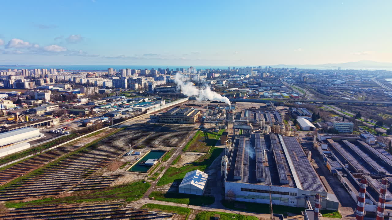 Horizonte urbano con zona industrial y humo elevándose de una fábrica durante el día.