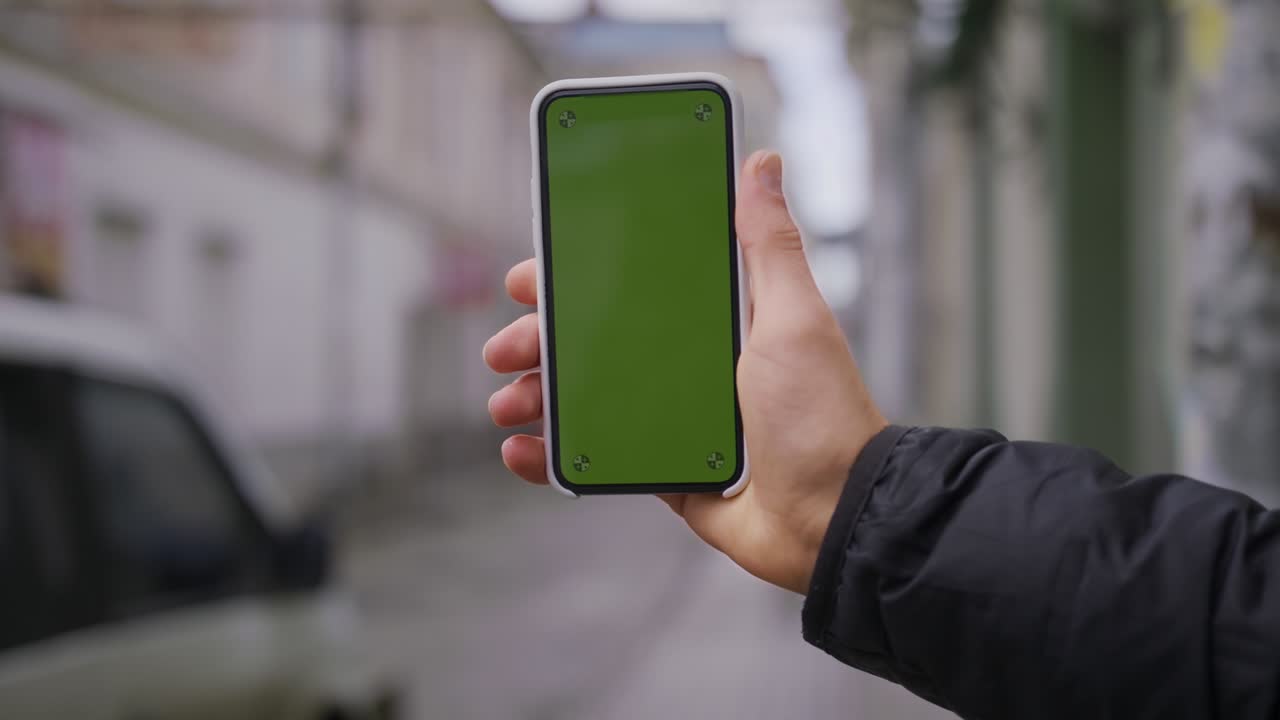 Hand man uses holding a mobile telephone with a vertical green screen background on of street houses people key smartphone technology touch message display