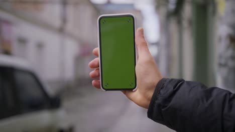 hand man uses holding a mobile telephone with a vertical green screen background on of street houses people key smartphone technology touch message display