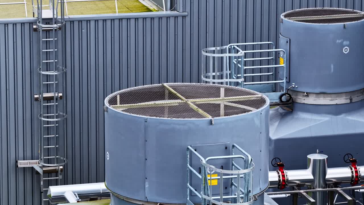 Zbliżenie na przemysłowe wieże chłodnicze i metalowe drabiny na tle ściany z blachy falistej. Idealne do wizualizacji procesów produkcyjnych lub przemysłowych.