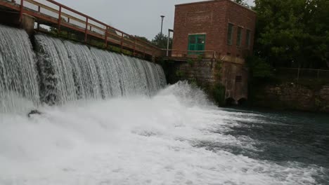 approaching bottom of water fall from dam flowing into river - drone angle