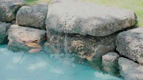 small water feature with clear blue water flowing gently over large stones, surrounded by a lush garden