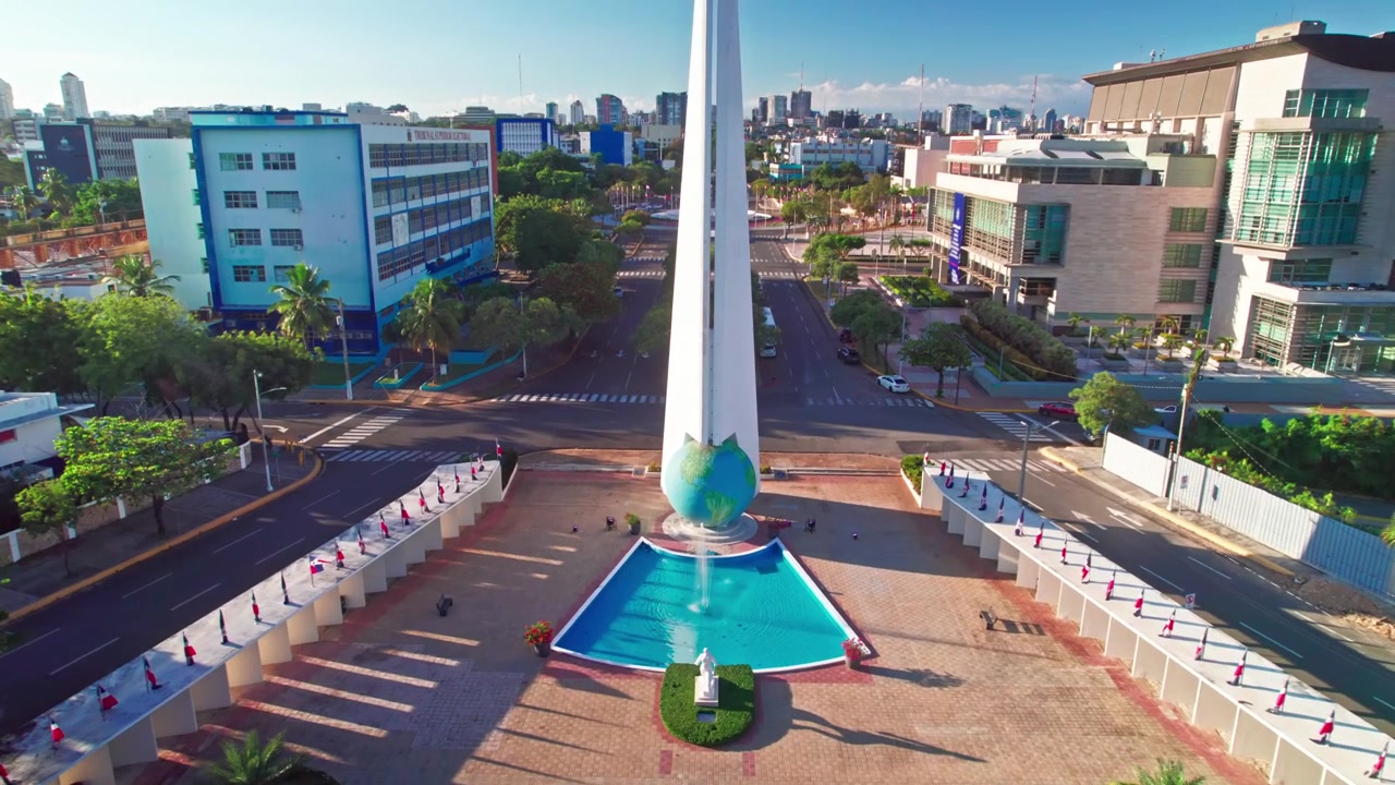 Ripresa aerea con drone dall'alto che avanza e scende sopra il monumento obelisco degli Eroi, la fontana della piazza centrale e gli edifici governativi circostanti a Santo Domingo