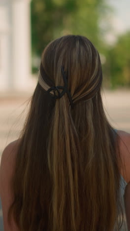 vista de fondo de cerca de una joven con el cabello rubio atado en un sello de cian negro, caminando tranquilamente por un camino entrelazado con un fondo escénico con edificios históricos, bancos, vegetación exuberante