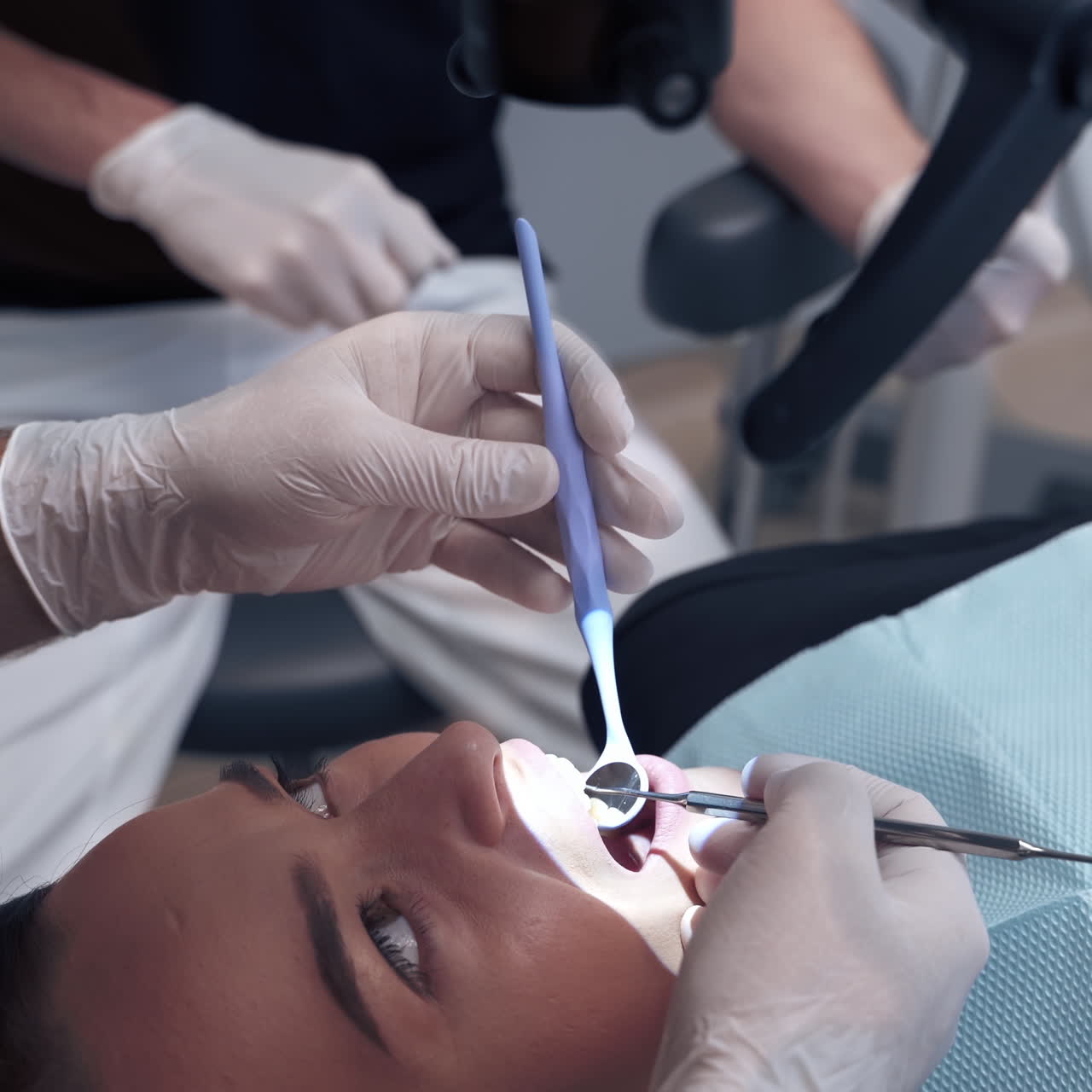 Dentist examines patient's teeth through the microscope. Specialist looks into female's mouth with medical tools in a dental office.