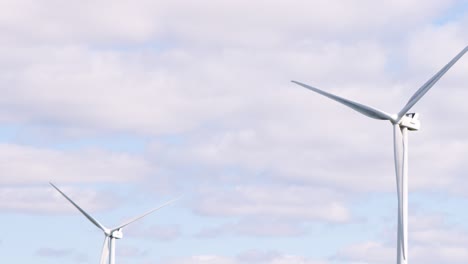 large wind turbines slowly rotate under partly cloudy skies in a rural field near edinburgh, scotland, captured in a steady, wide shot with natural daylight