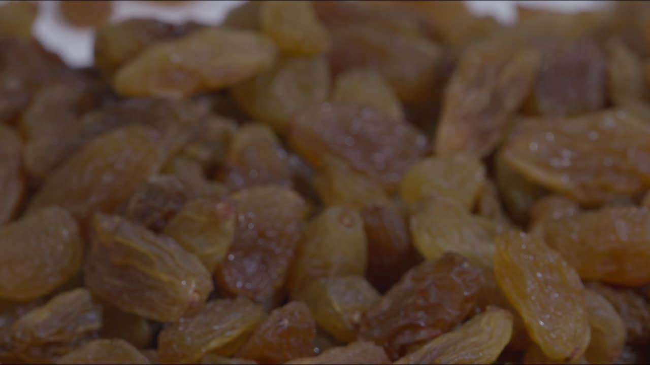 A steady and very slow zoom out shot of Golden Raisins on a table