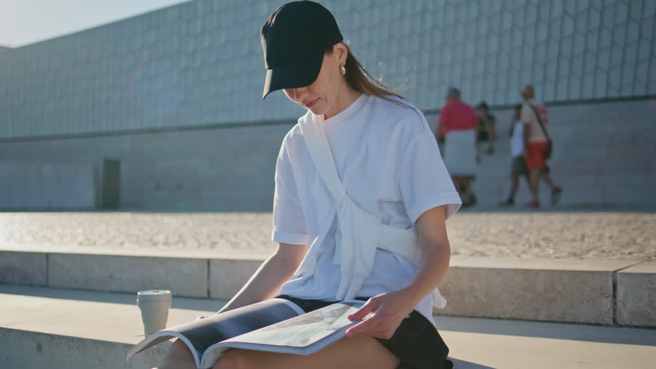 Relaxed woman flipping pages magazine sitting sunny street with coffee cup