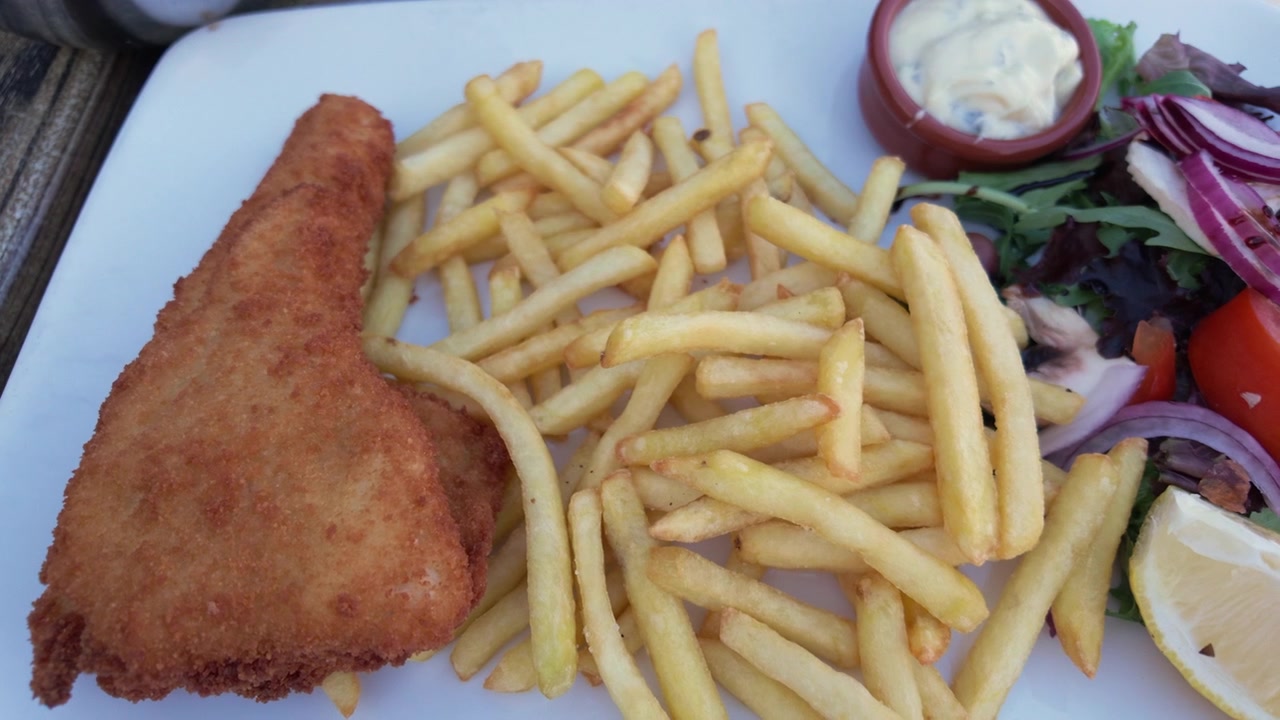 Primo piano di un filetto di pesce impanato con patatine fritte, insalata, salsa tartara e uno spicchio di limone