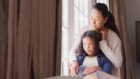 video of thoughtful asian mother and daughter looking outside window