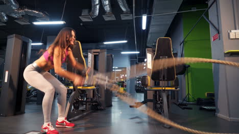 battle ropes session. attractive young and athletic girl using training ropes in a gym.