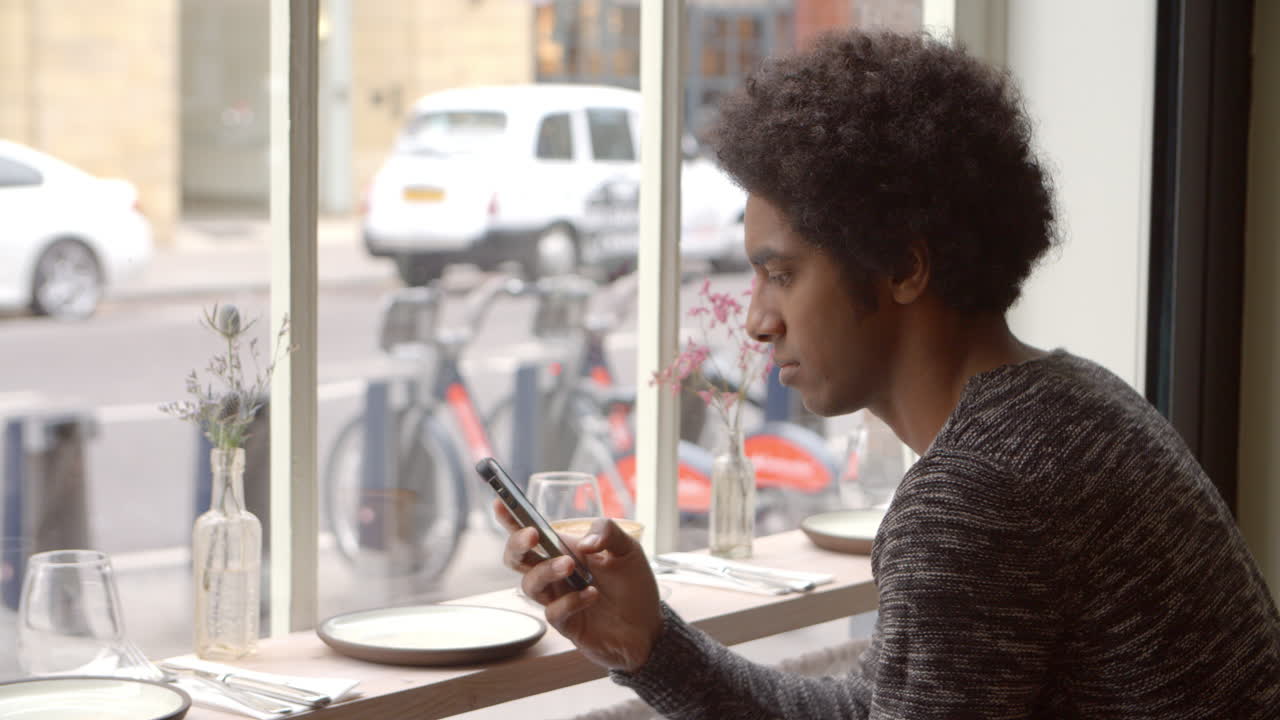 Young Man Using Mobile Phone To Update Social Media In Cafe