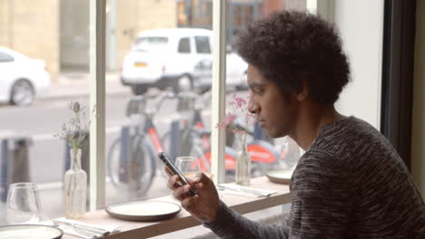 Un-Joven-Que-Usa-Un-Teléfono-Móvil-Para-Actualizar-Las-Redes-Sociales-En-La-Cafetería.