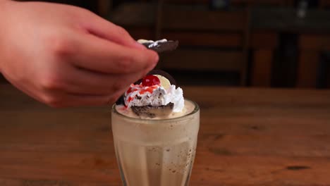 Detailed-close-up-of-chocolate-milkshake,-with-caramel,-espresso-coffee-and-whipped-cream-with-cherry,-hand-taking-whipped-cream-with-a-chocolate-cookie