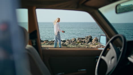 mujer junto al océano, vista desde dentro de un coche de época