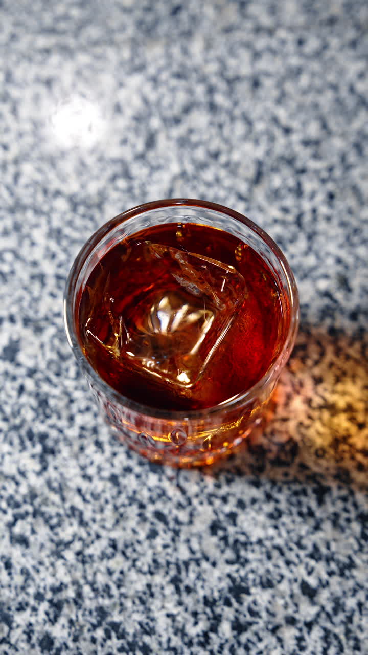 Metal tongs are used to put lemon peel on top of the glass. Serving the beverage with ice cube in a bar. Top view. Vertical video.