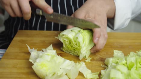 cutting green fresh cabbage with kitchen knife on wooden cut board