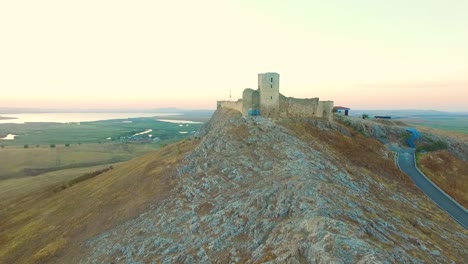 Fortaleza-De-Enisala-En-Rumania,-Disparo-De-Drones,-Volando-Lejos-De-La-Fortaleza-Al-Atardecer