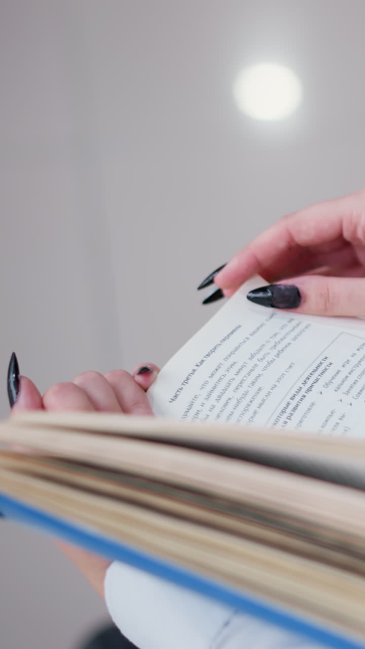 vista parcial trasera de una mujer leyendo un libro mientras está sentada en un banco, el reflejo de la luz en los azulejos crea un ambiente suave, las uñas pulidas negras contrastan con las páginas nítidas