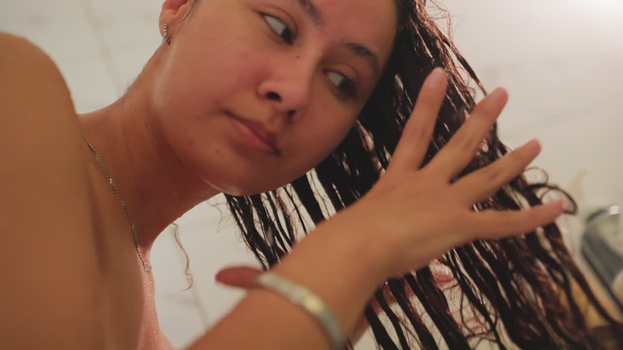 Gentle shower detangle and style. Relaxed individual smoothing long curls while washing hair carefully. Person delicately detangles wet hair under shower spray focusing on styling and grooming