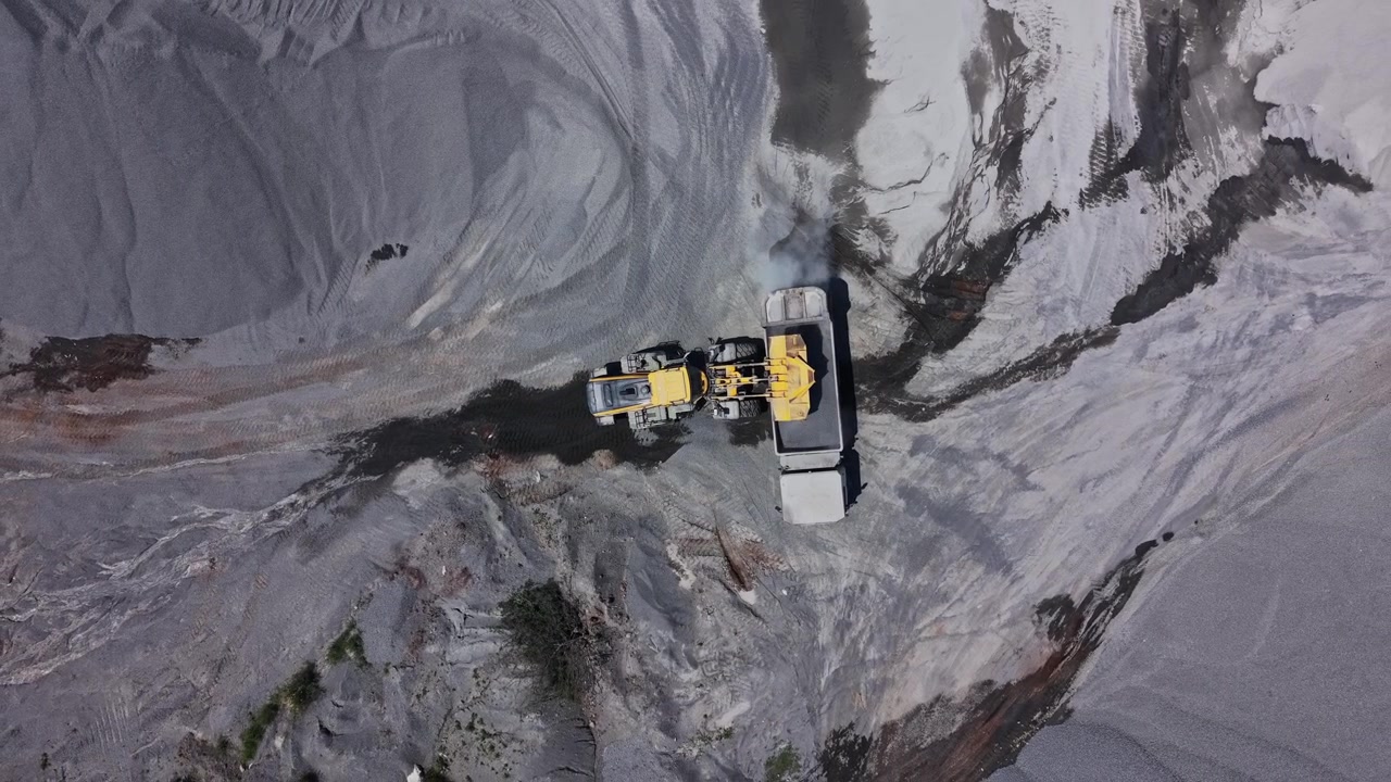Heavy machinery moves gravel at construction site in daylight
