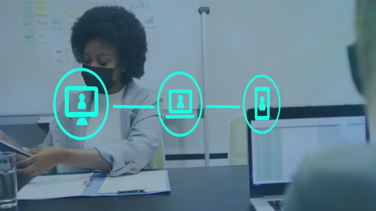Animation of network of digital icons over two diverse women wearing face masks discussing at office